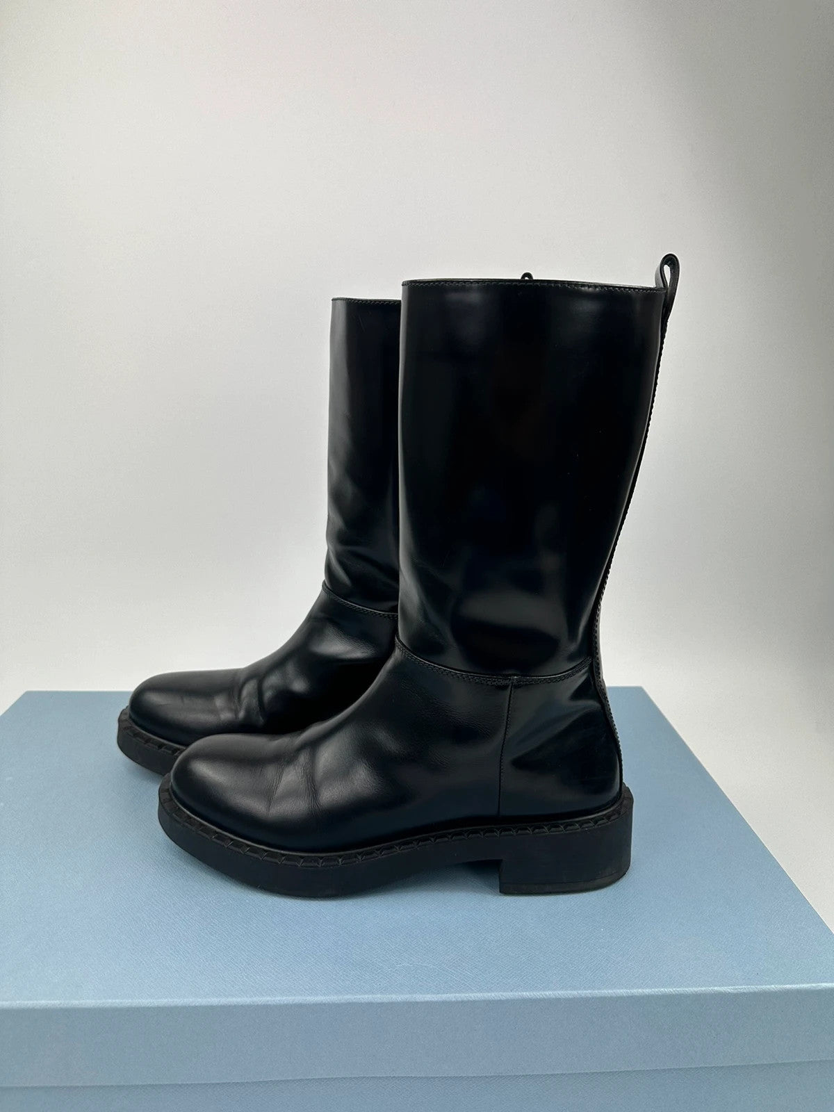 Prada black knee-high boots in patent leather with logo detail and elegant design.