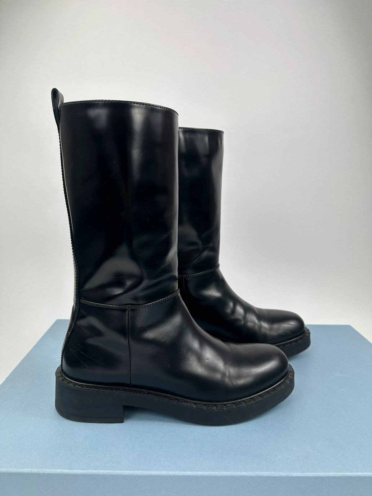 Prada black knee-high boots in patent leather with logo detail and elegant design.