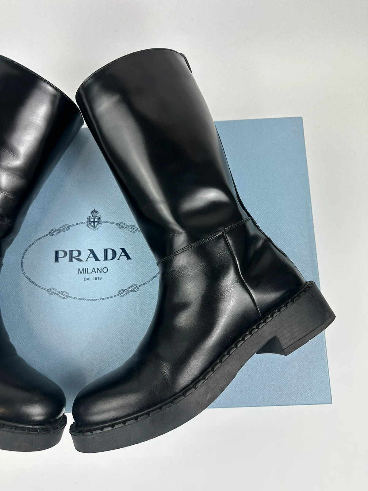 Prada black knee-high boots in patent leather with logo detail and elegant design.