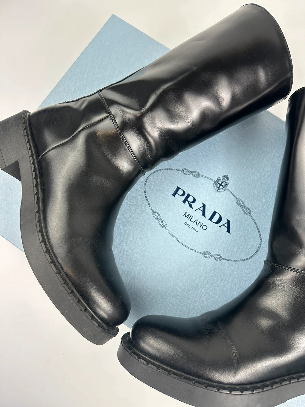 Prada black knee-high boots in patent leather with logo detail and elegant design.
