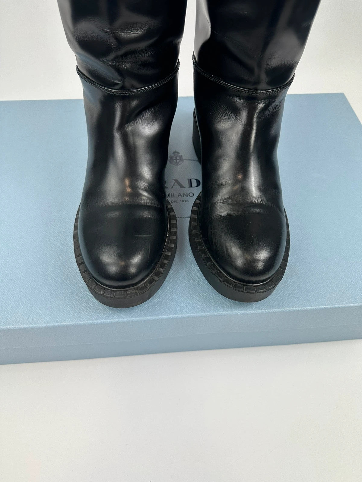 Prada black knee-high boots in patent leather with logo detail and elegant design.