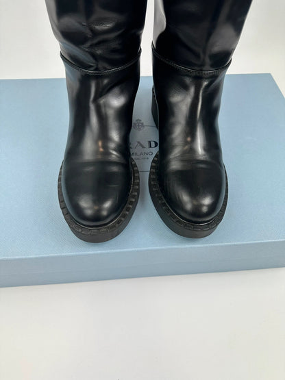 Prada black knee-high boots in patent leather with logo detail and elegant design.