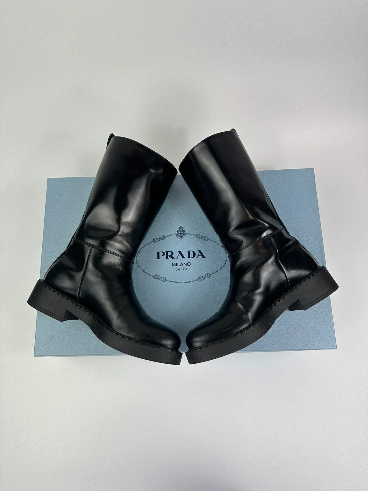 Prada black knee-high boots in patent leather with logo detail and elegant design.