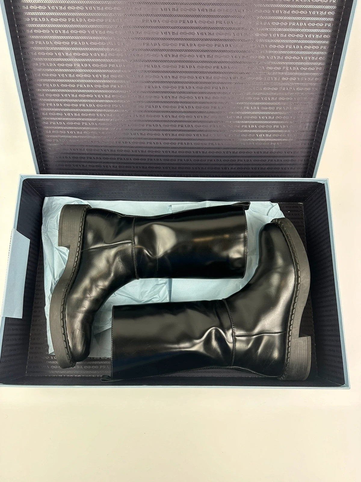 Prada black knee-high boots in patent leather with logo detail and elegant design.