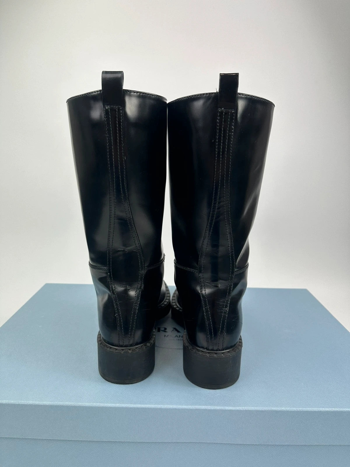 Prada black knee-high boots in patent leather with logo detail and elegant design.
