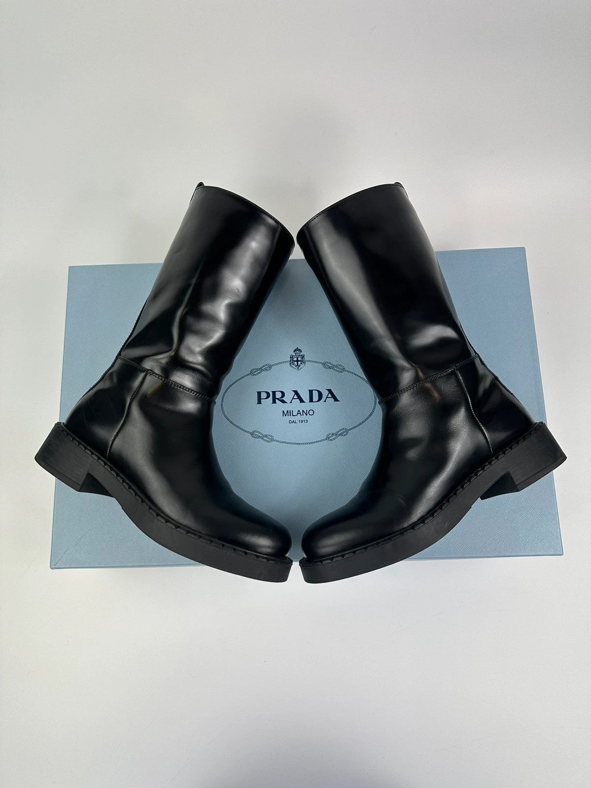 Prada black knee-high boots in patent leather with logo detail and elegant design.