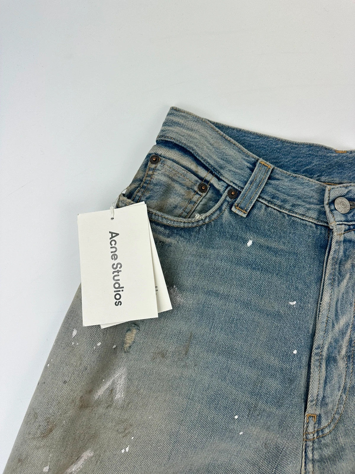 Acne Studios blue and white baggy jeans with intentional paint splatters and non-stretch denim.