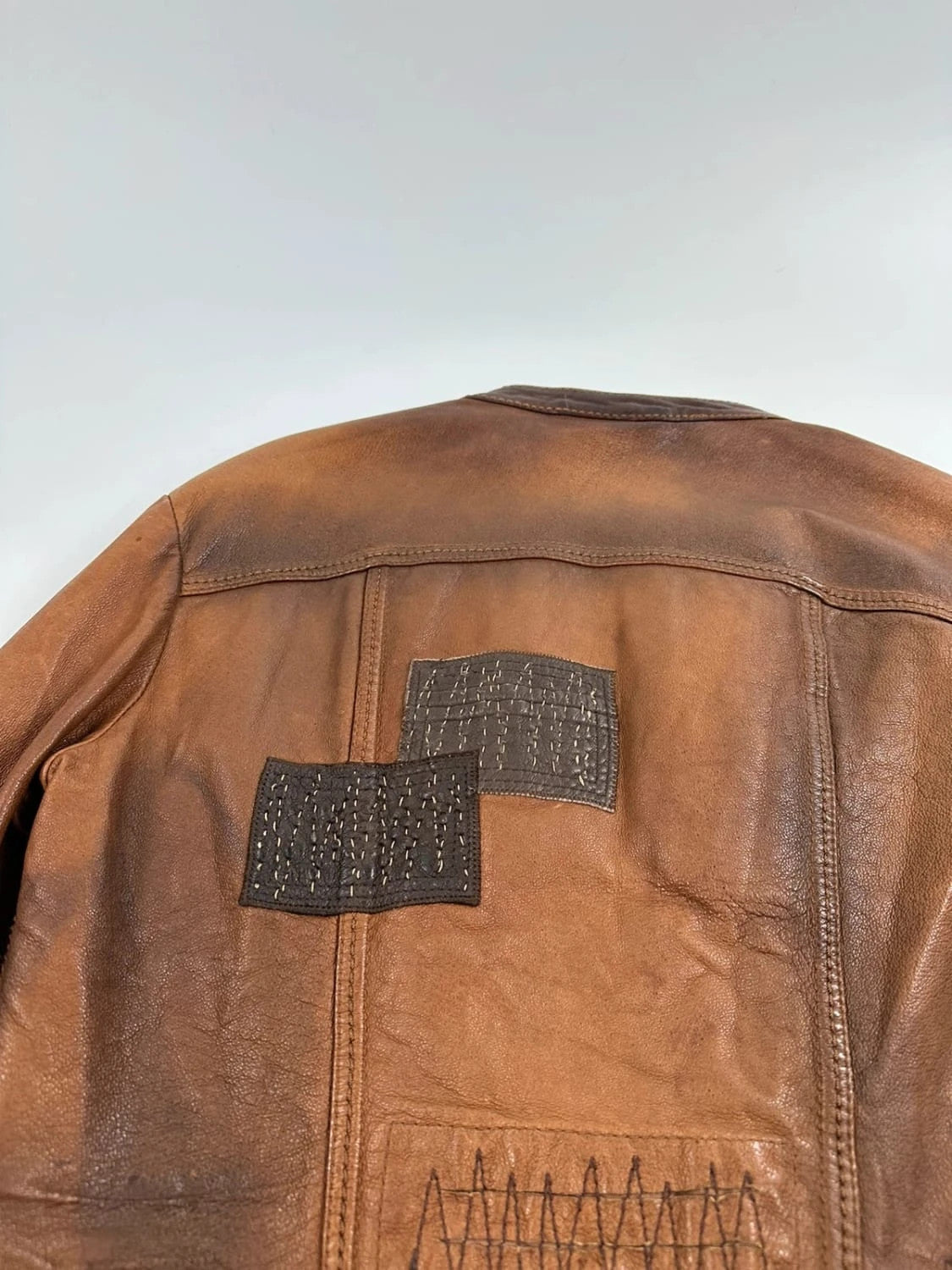 Marithé Francois Girbaud brown leather jacket with orange patches and logo details.