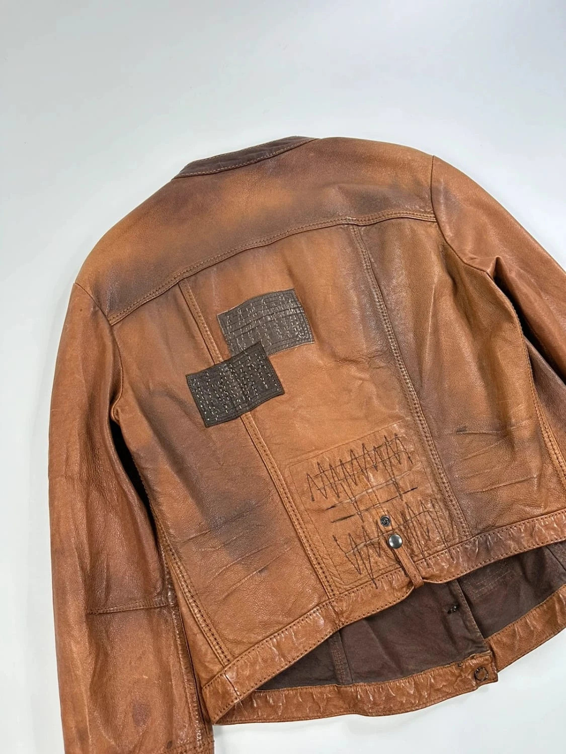 Marithé Francois Girbaud brown leather jacket with orange patches and logo details.