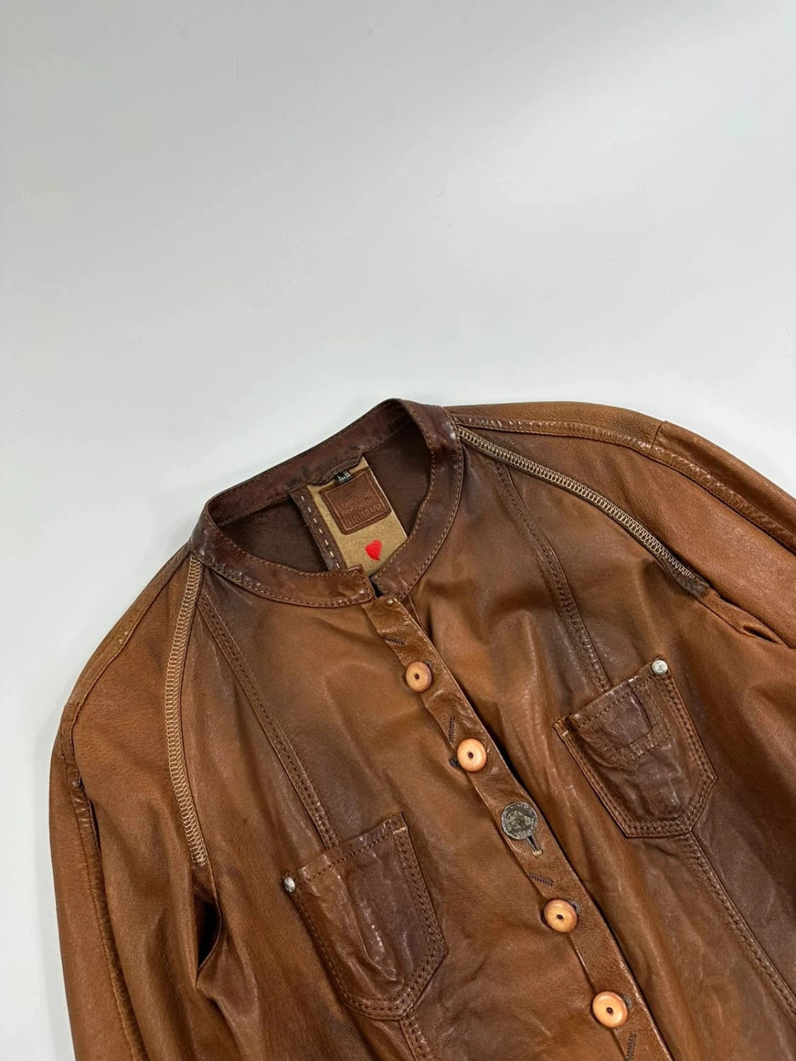 Marithé Francois Girbaud brown leather jacket with orange patches and logo details.