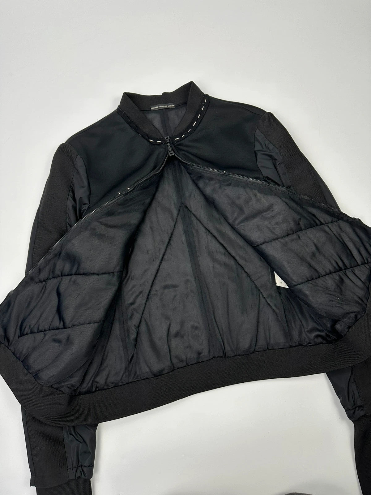 Marithé Francois Girbaud black coat with white utility stitching and logo details.