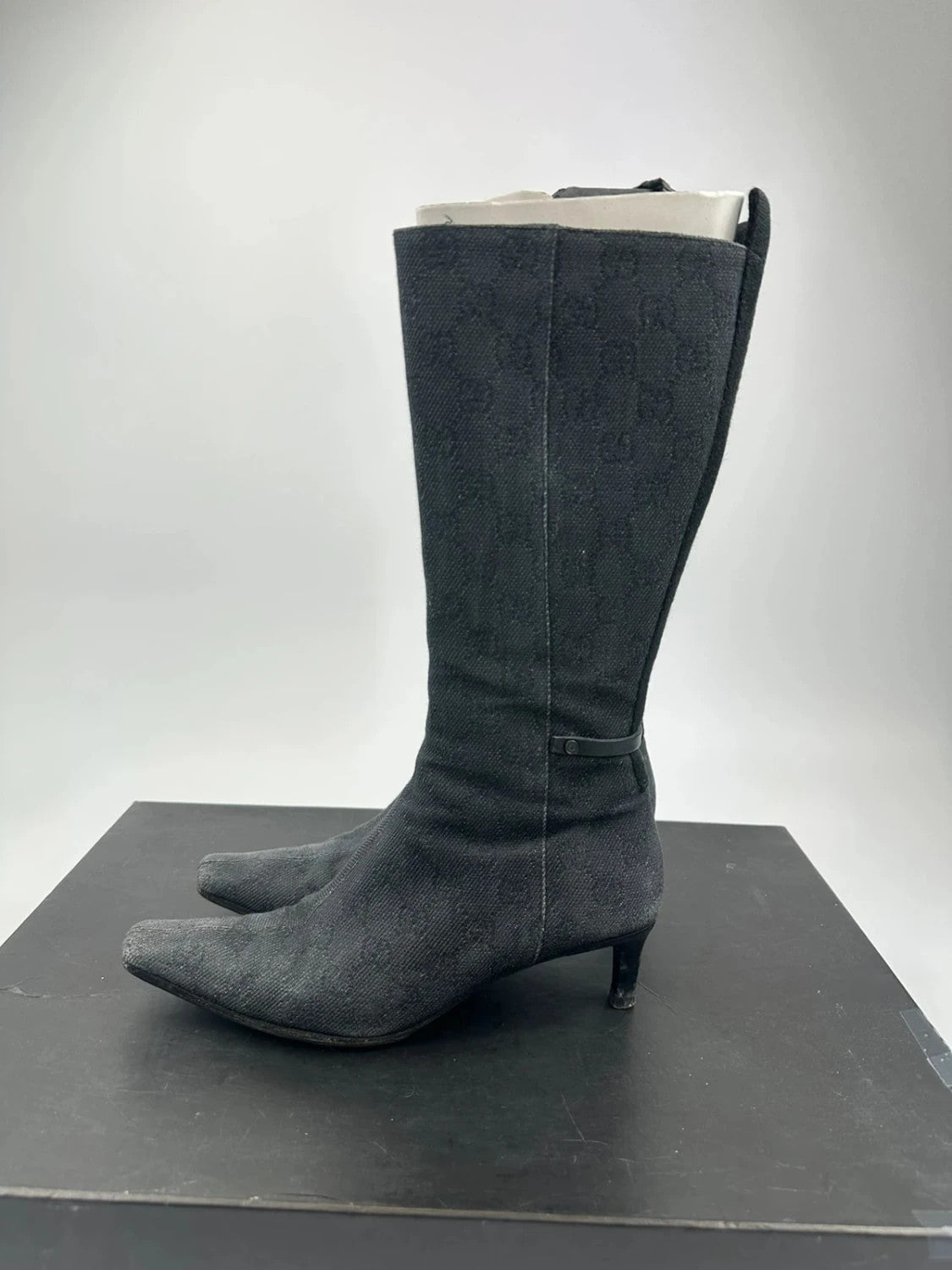 Gucci black monogram knee-high boots with pointed toe and logo pattern.