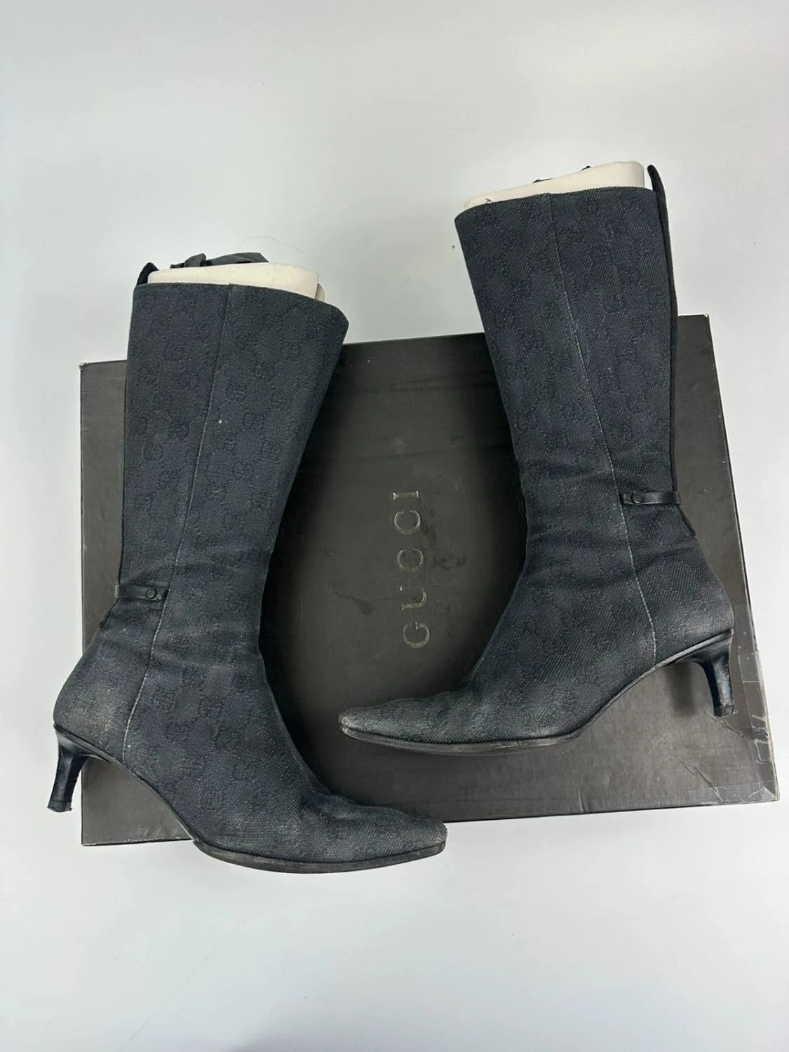 Gucci black monogram knee-high boots with pointed toe and logo pattern.