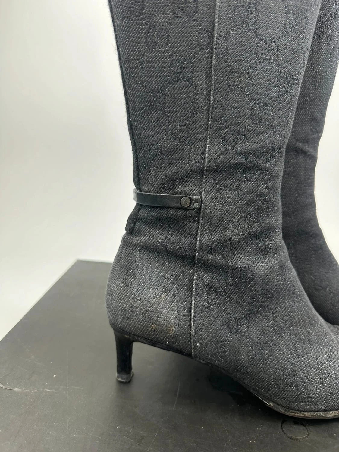 Gucci black monogram knee-high boots with pointed toe and logo pattern.