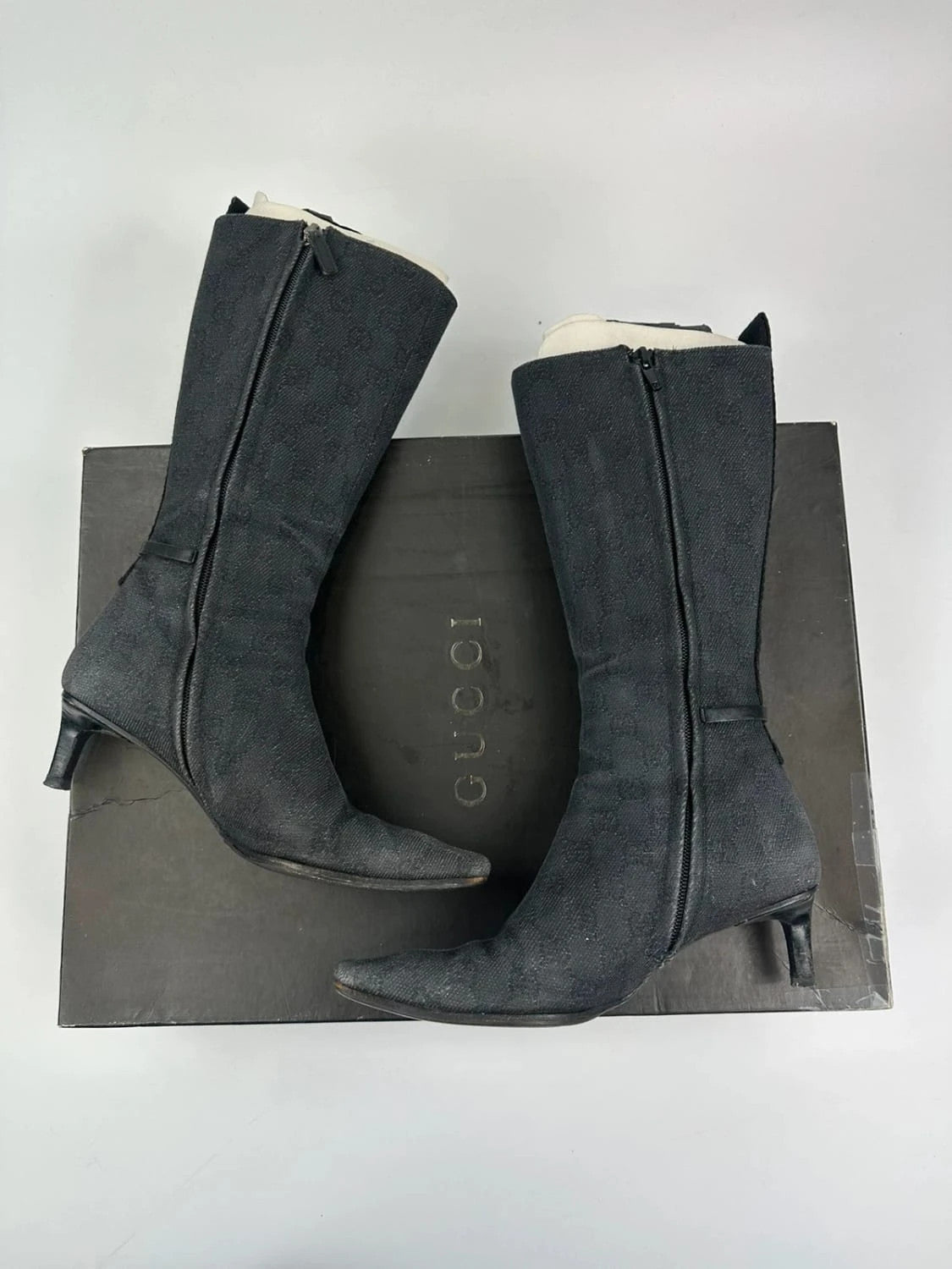 Gucci black monogram knee-high boots with pointed toe and logo pattern.
