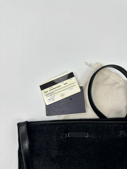 Prada black leather crossbody bag with fur accents and embossed logo.
