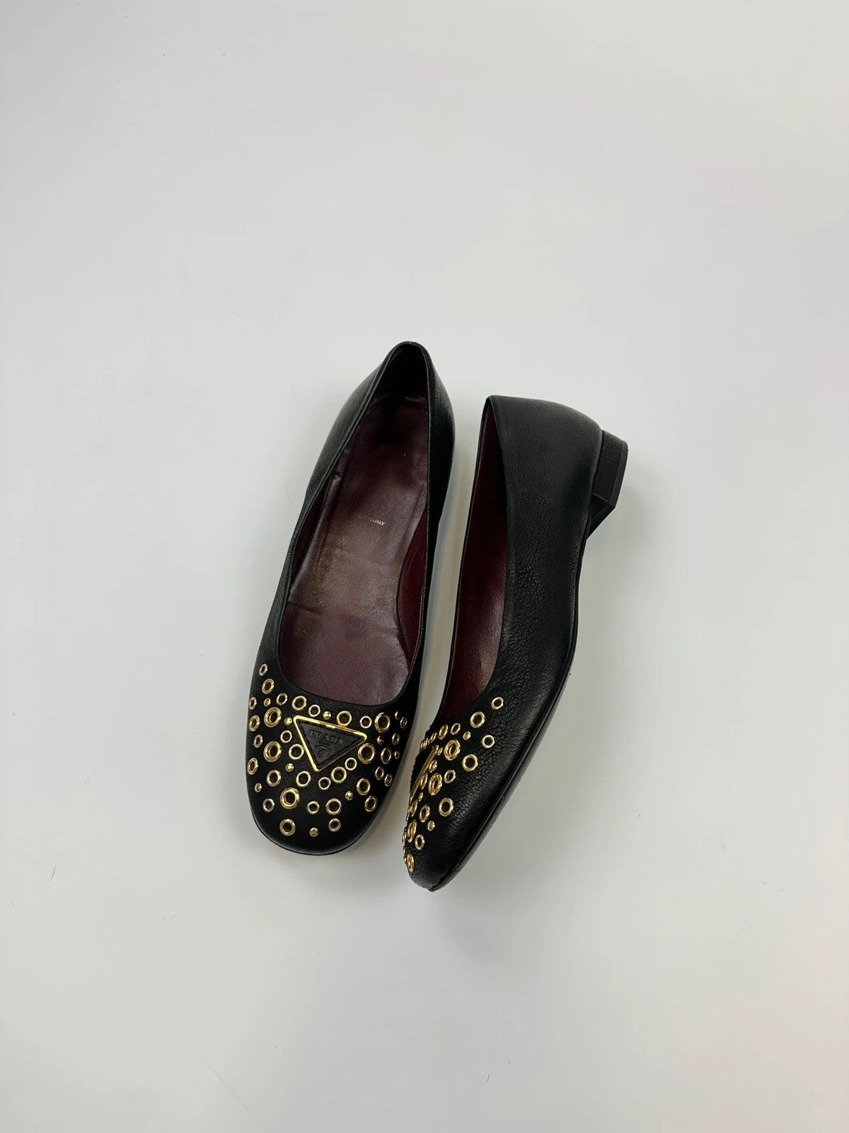 Prada black grained leather loafers with gold eyelets and triangle logo.