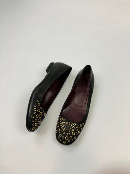 Prada black grained leather loafers with gold eyelets and triangle logo.