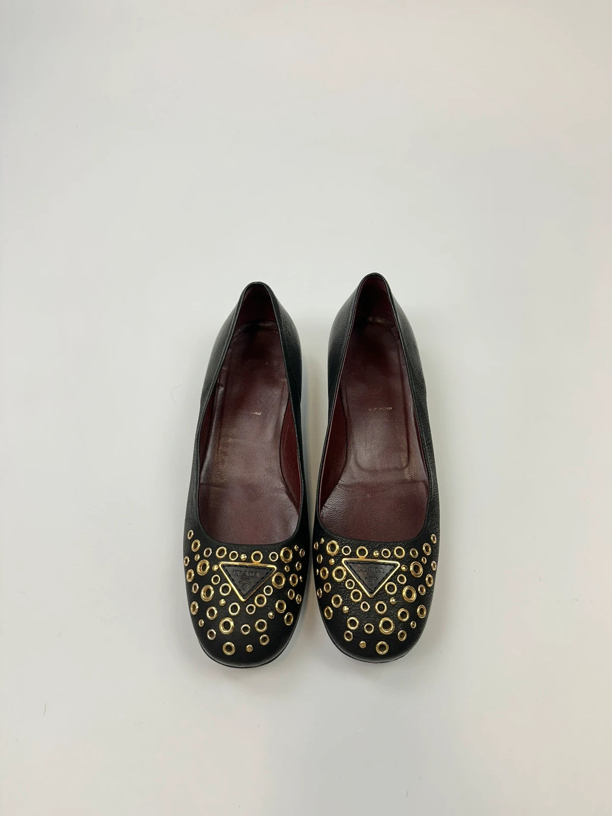 Prada black grained leather loafers with gold eyelets and triangle logo.