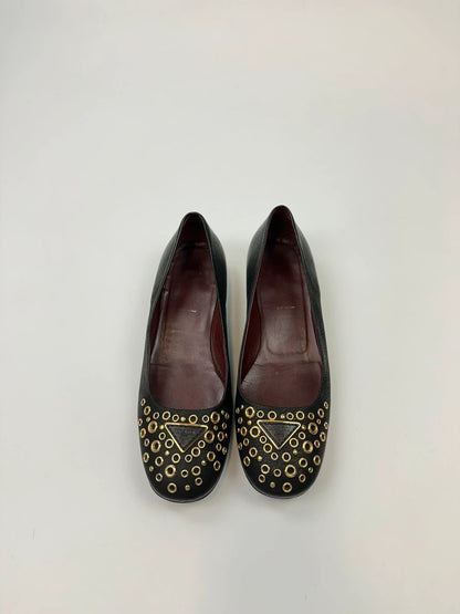 Prada black grained leather loafers with gold eyelets and triangle logo.