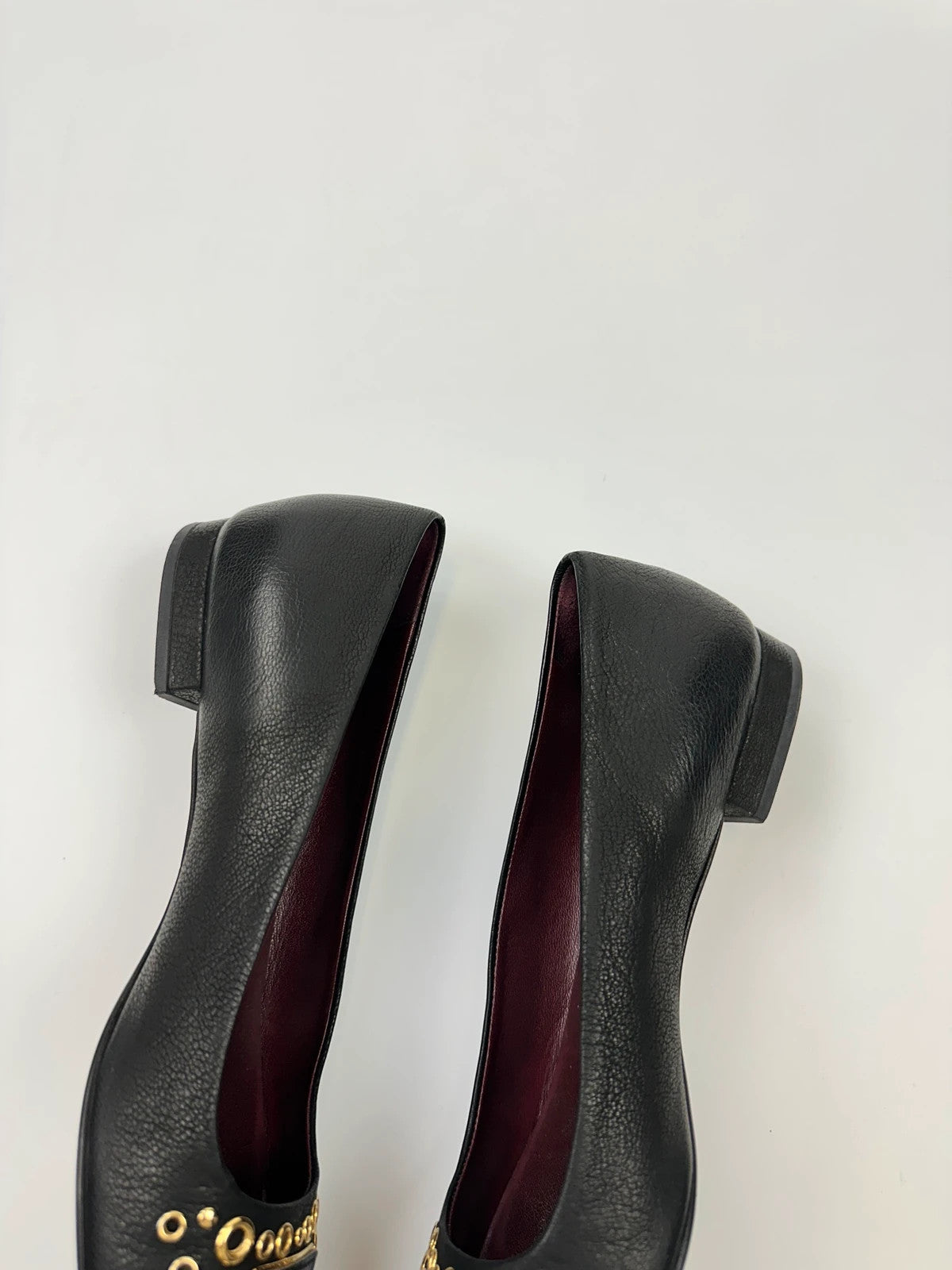 Prada black grained leather loafers with gold eyelets and triangle logo.