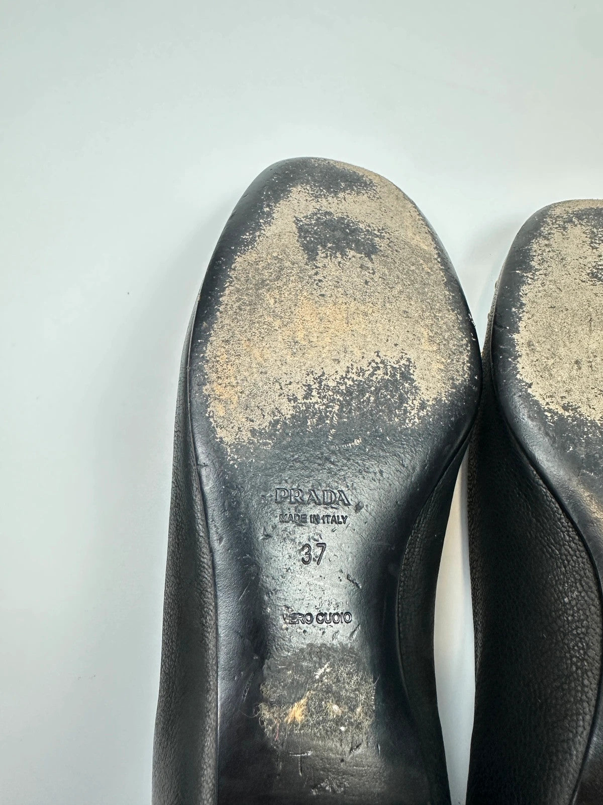 Prada black grained leather loafers with gold eyelets and triangle logo.