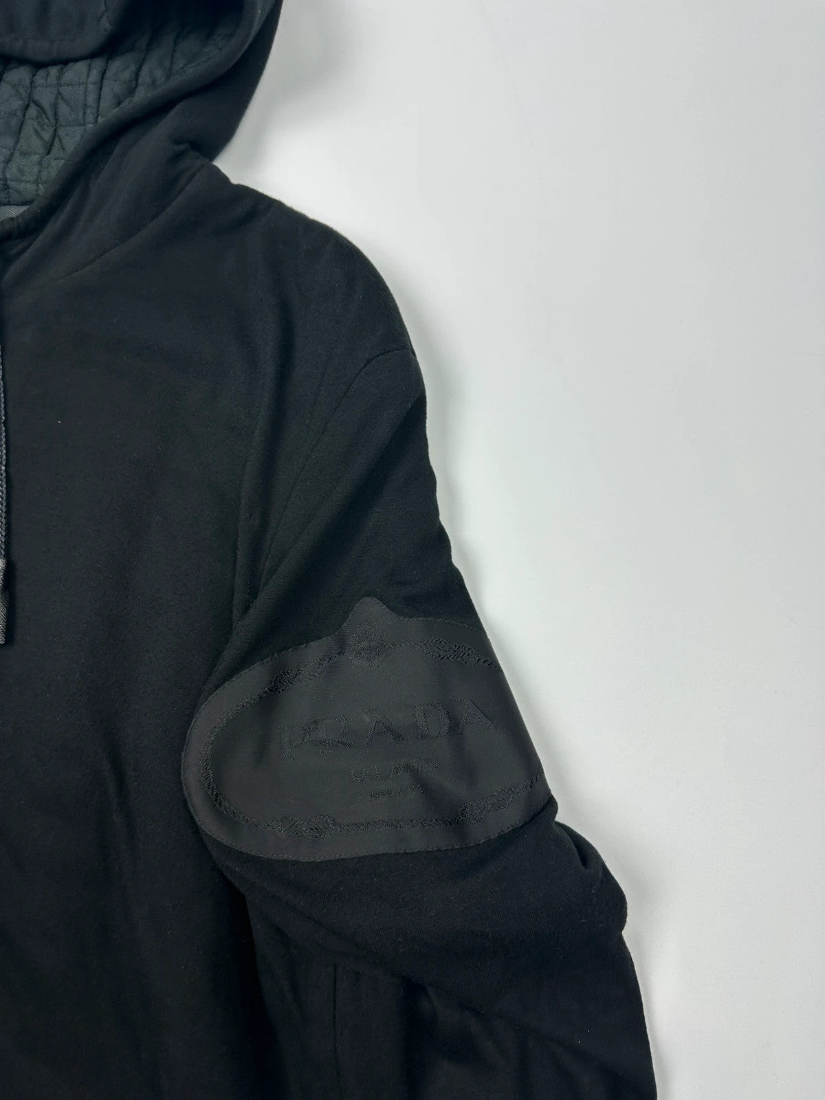Prada black padded hooded jacket with 90s-inspired patch and braided drawstrings.
