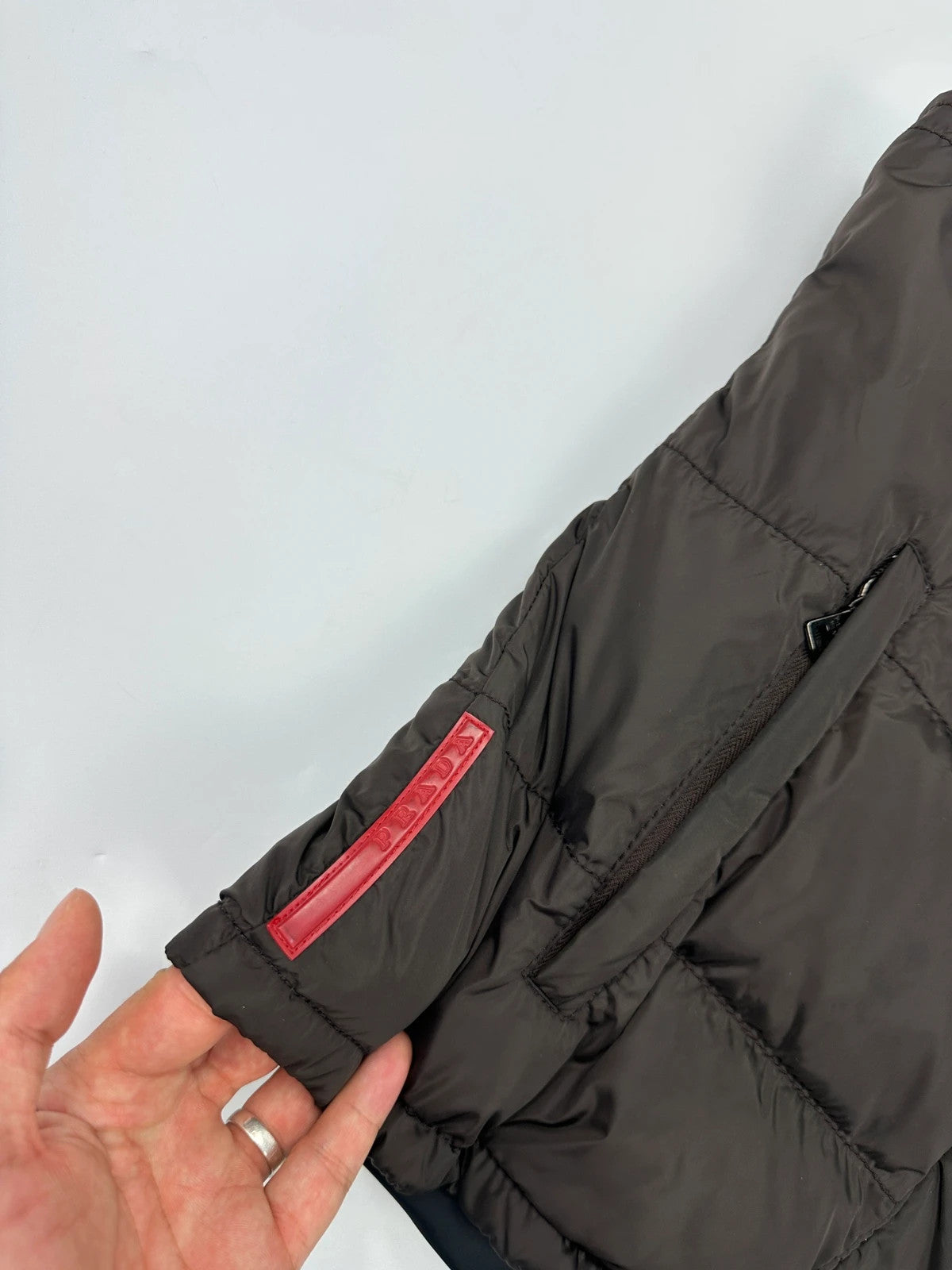 Prada brown puffer vest with retractable hood and linearossa logo details.
