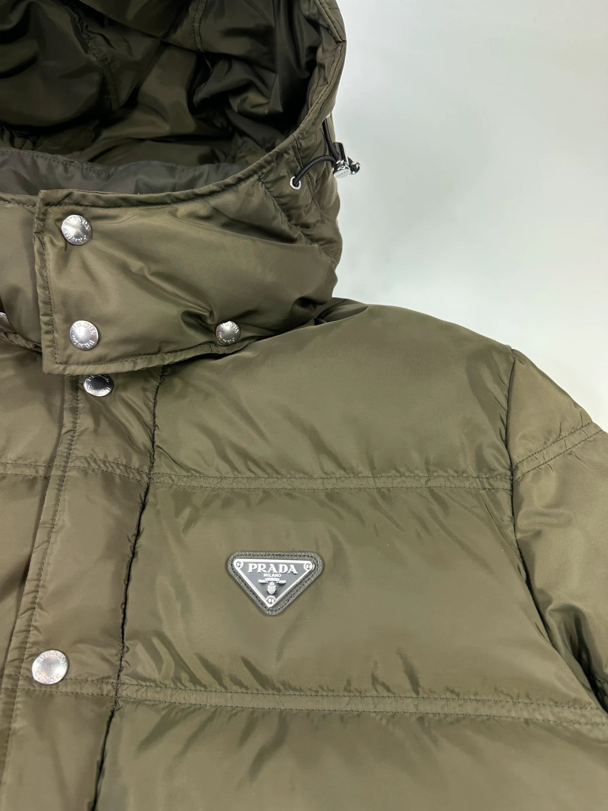 Prada khaki puffer down jacket with hood, featuring triangle logo and luxurious material.