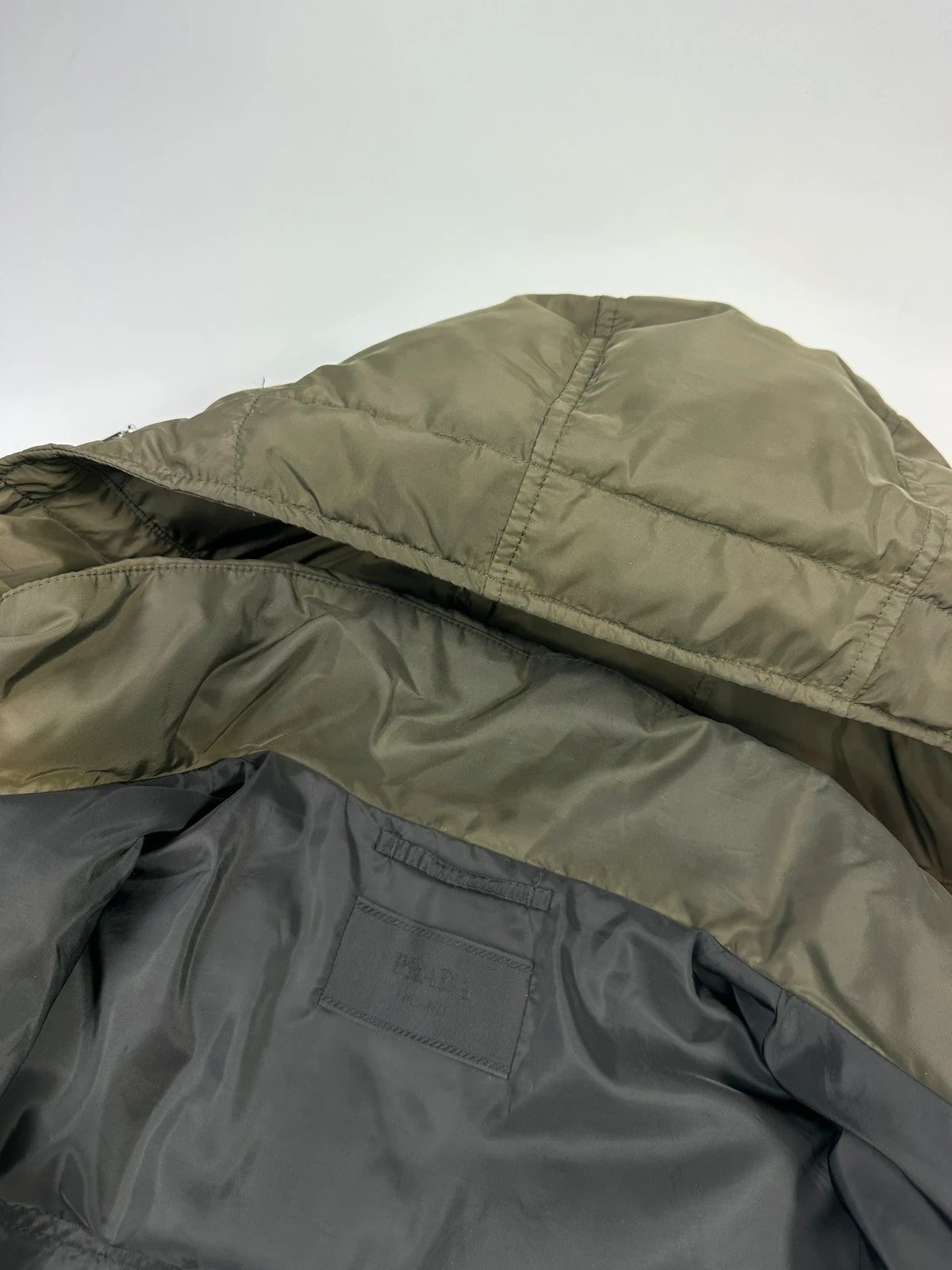 Prada khaki puffer down jacket with hood, featuring triangle logo and luxurious material.