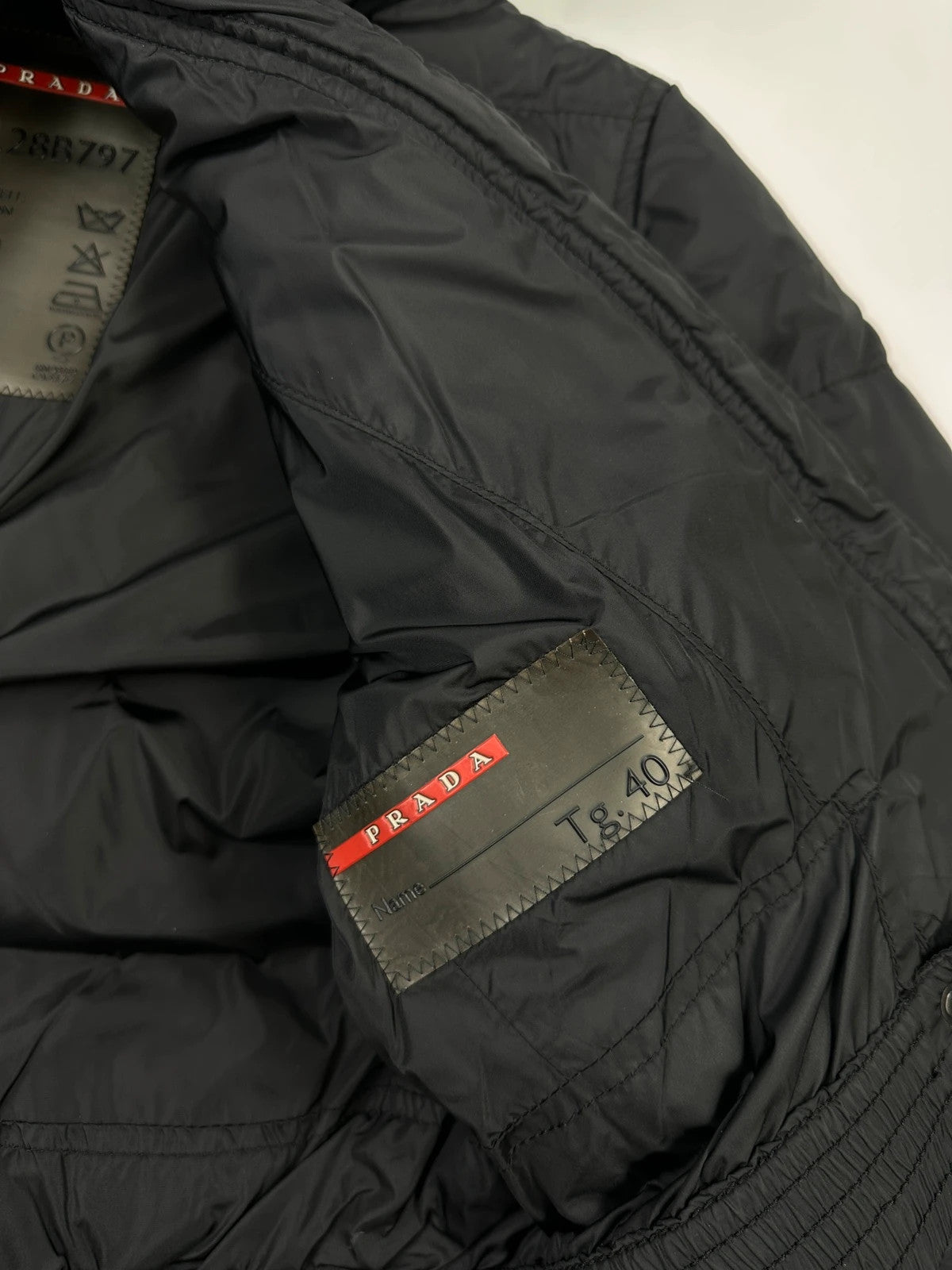 Prada black fitted nylon down puffer jacket with hood and logo detail.