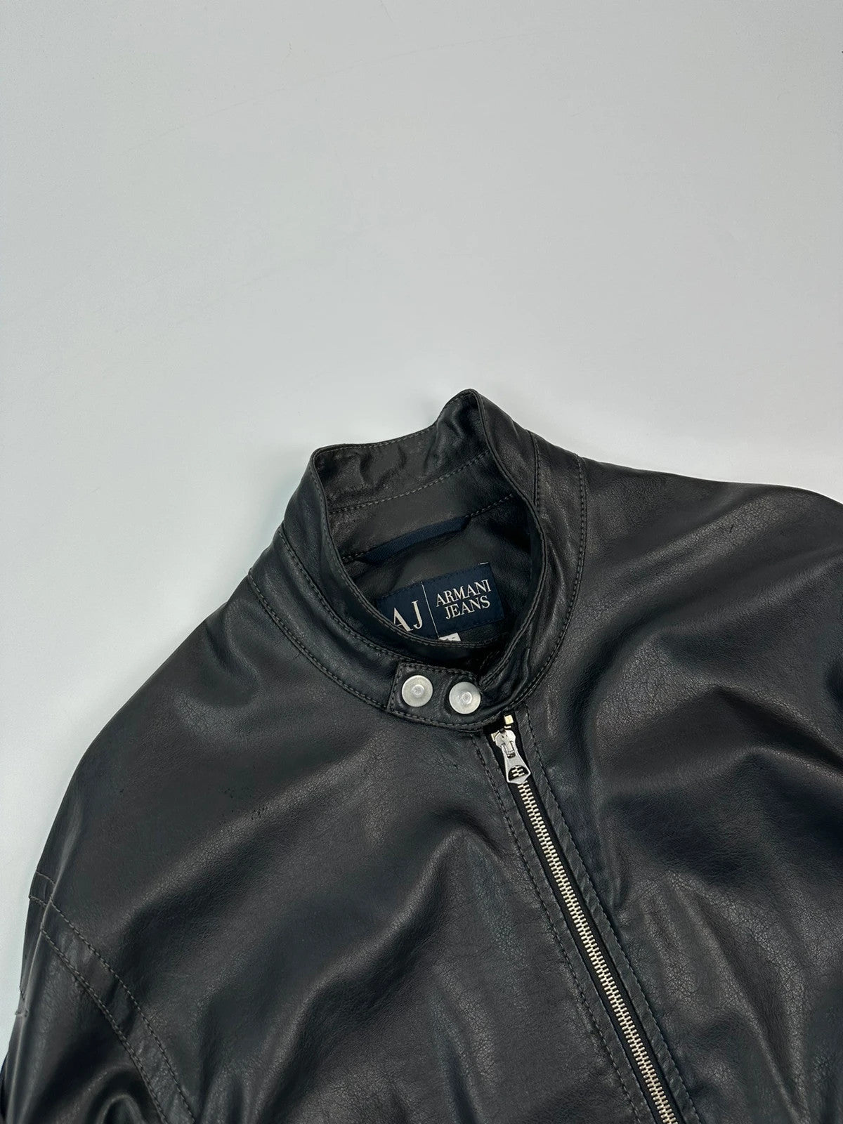Armani Jeans black faux leather jacket with worn pockets and minimalist design.