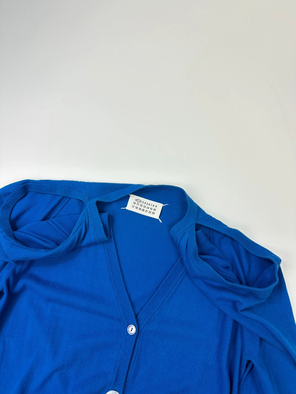 Maison Margiela electric blue cardigan with shoulder holes, minimalist design, soft knit material.