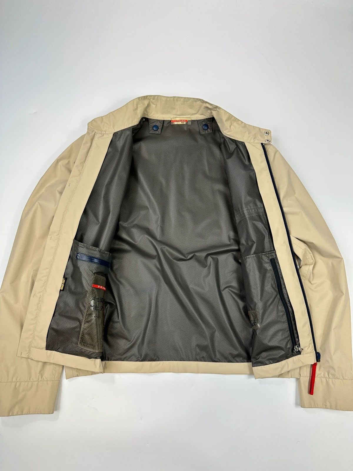 Prada beige Gore-Tex jacket packable into pocket, features logo and nylon material.