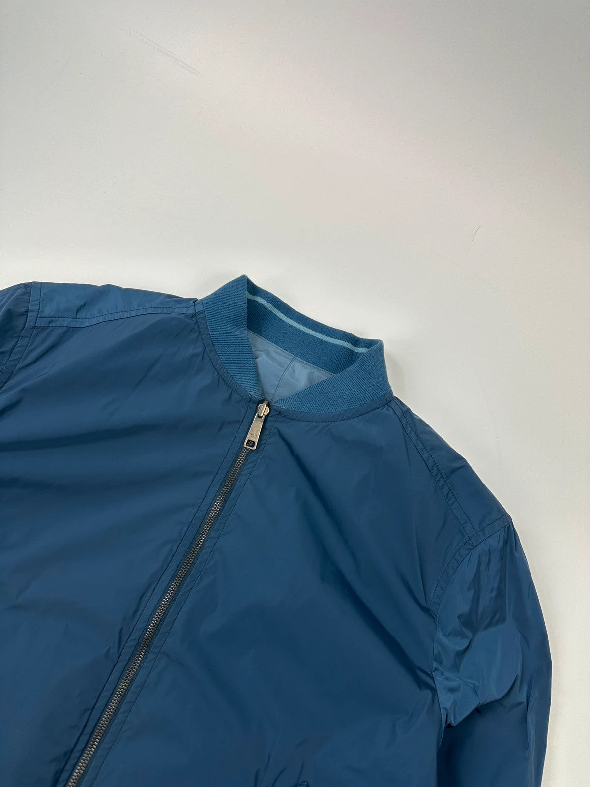 Prada blue reversible bomber jacket, nylon material, featuring logo and sleek minimalist design.