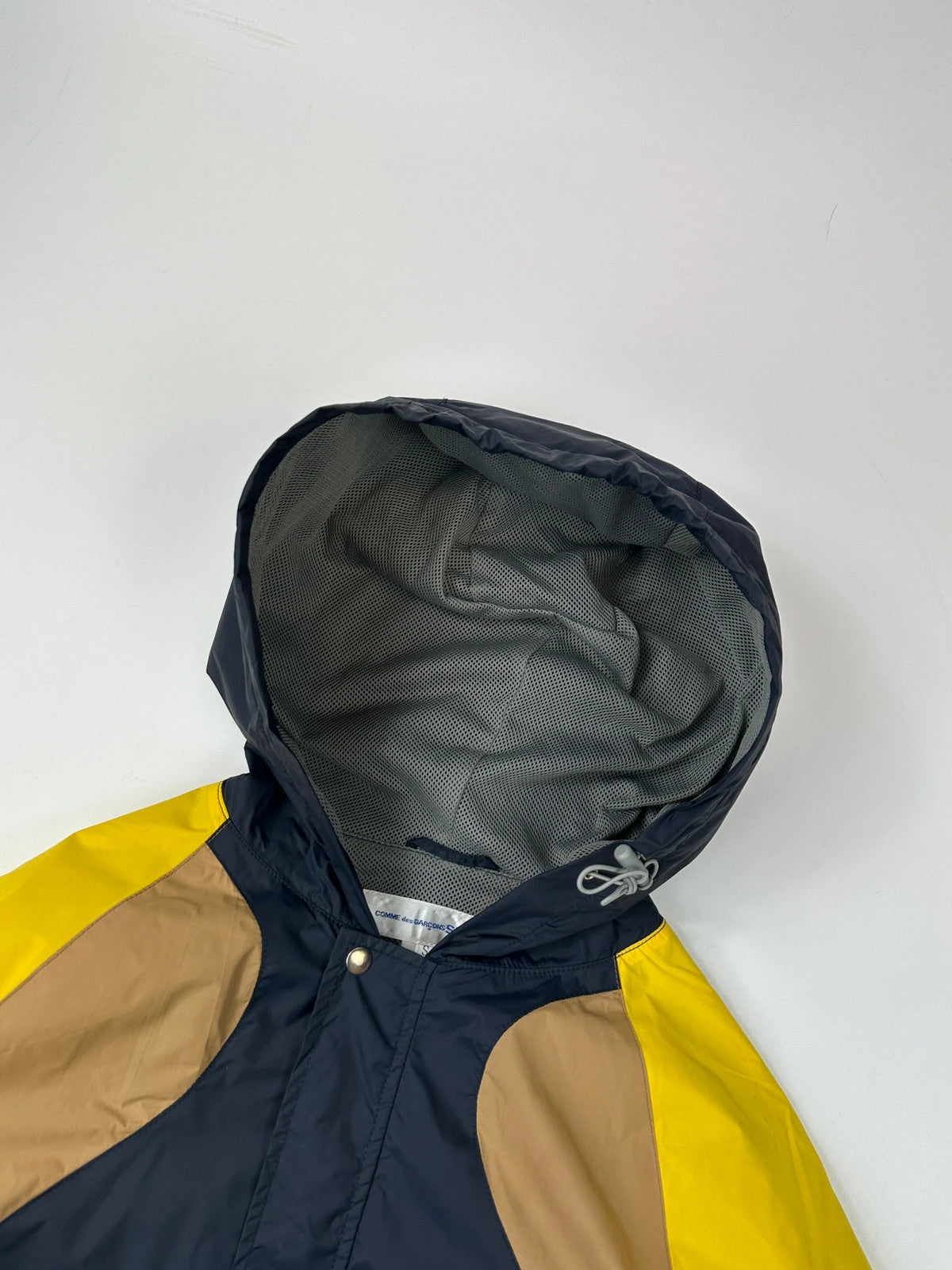 Comme Des Garçons navy and yellow block nylon hooded jacket with logo detail.